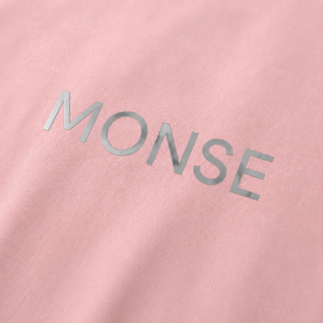 Close-up of the MONSE chrome wordmark on soft pink cotton