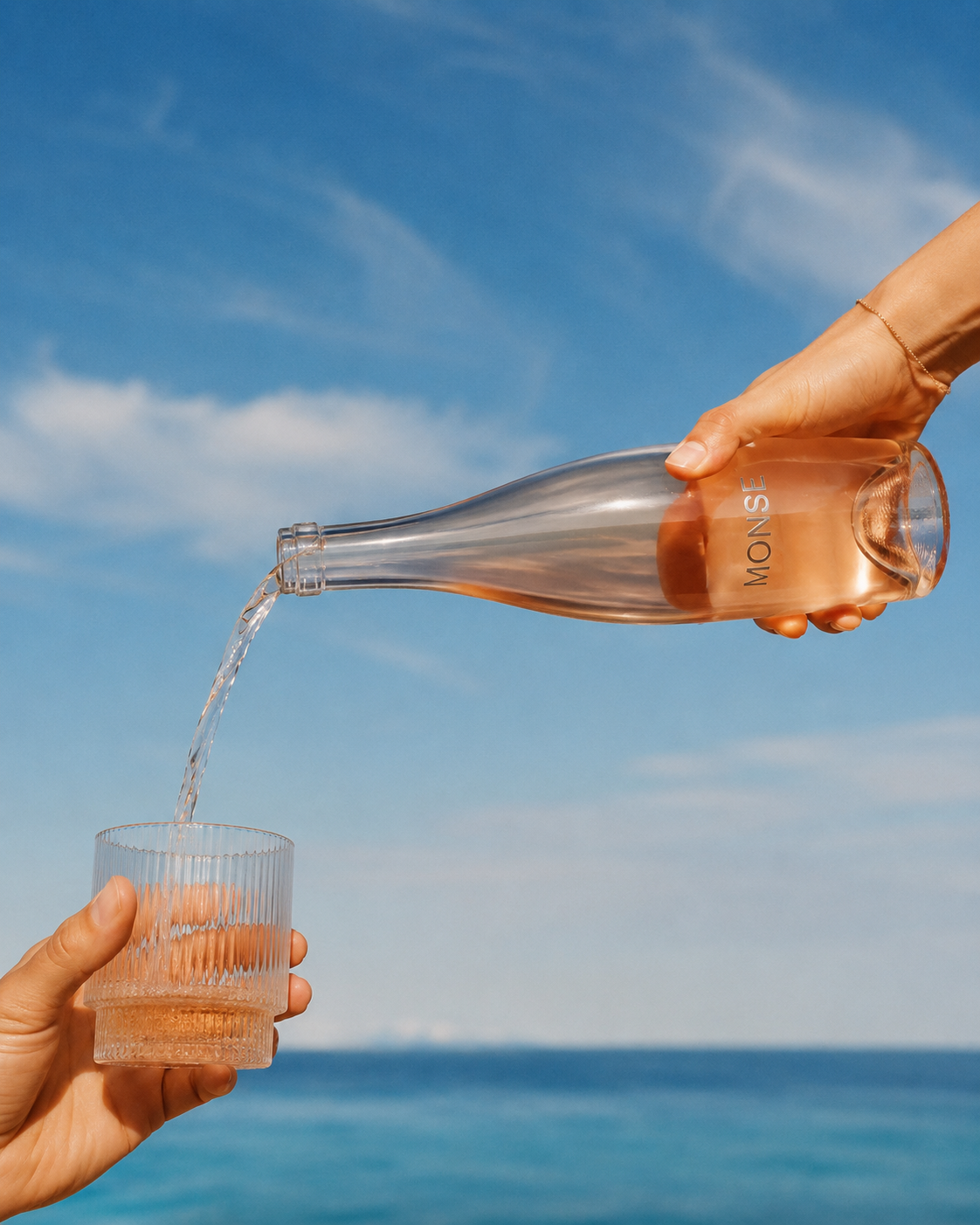 A bottle of MONSE rosé being poured into a fluted glass against the ocean and sky